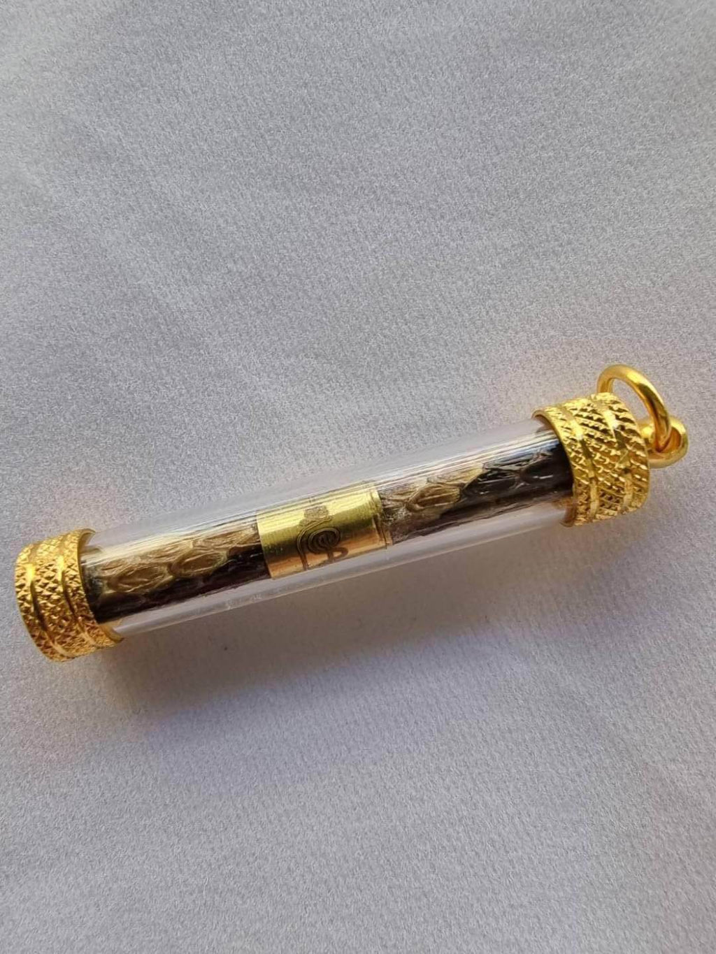 Python skin takrud amulet encased in clear tube with gold accents for protection and good fortune