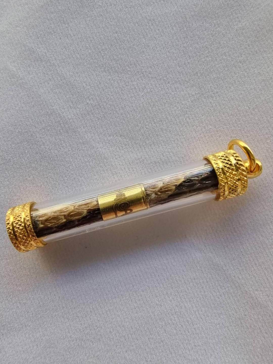 Python skin takrud amulet encased in clear tube with gold accents for protection and good fortune