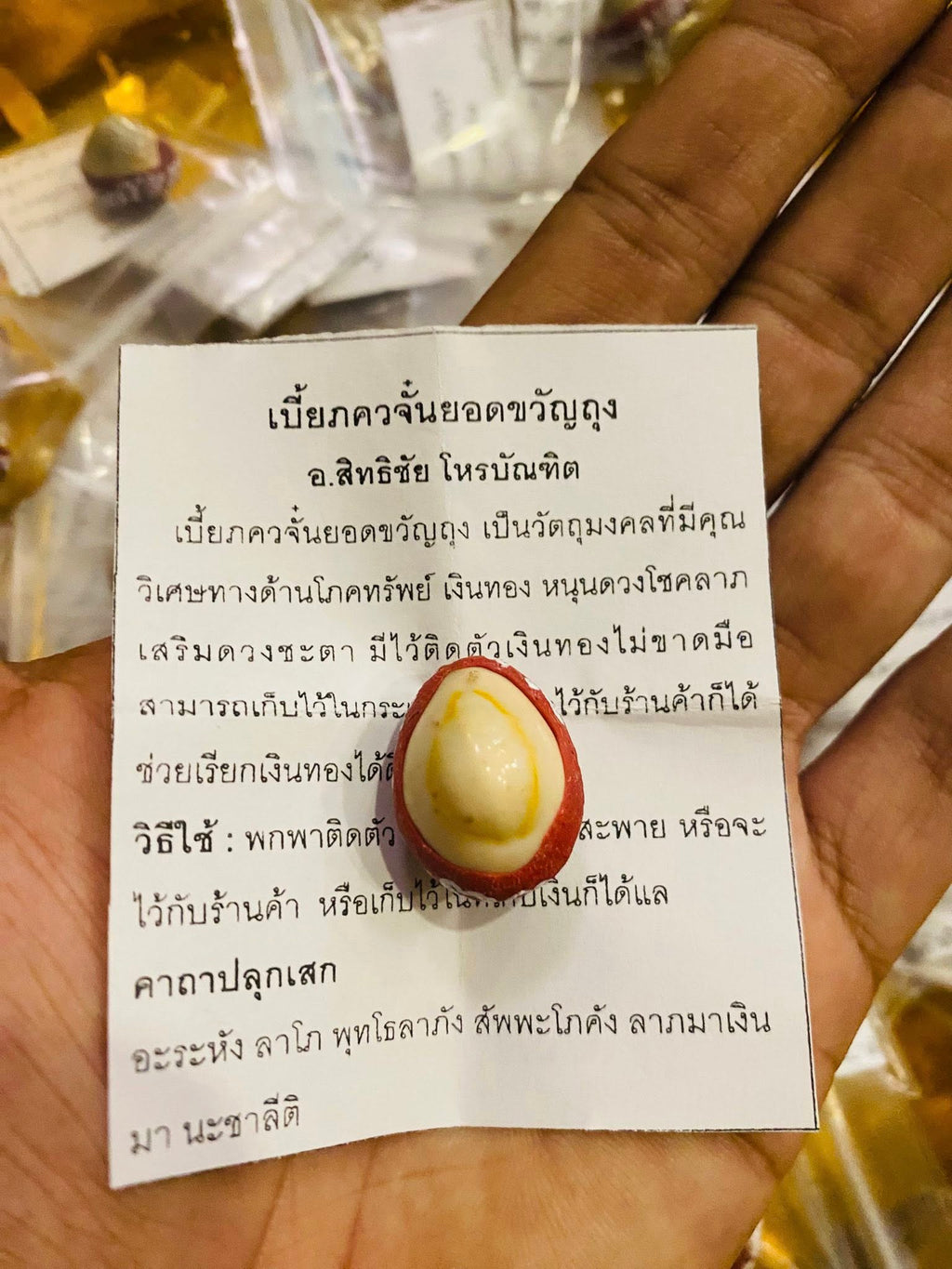 Hand holding Thai lucky millionaire amulet for wealth red and white egg shaped charm on blessing paper