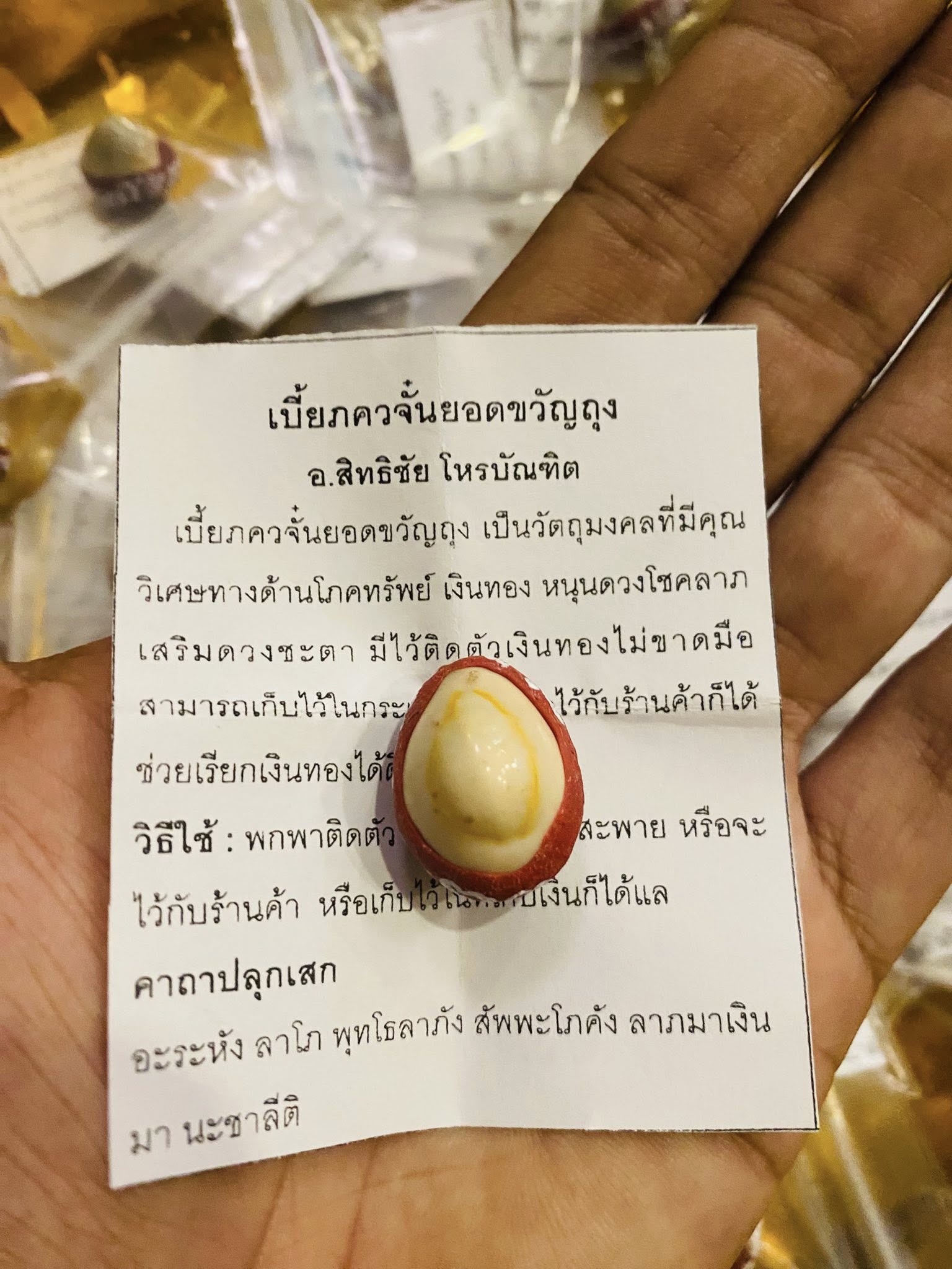 Hand holding Thai lucky millionaire amulet for wealth red and white egg shaped charm on blessing paper