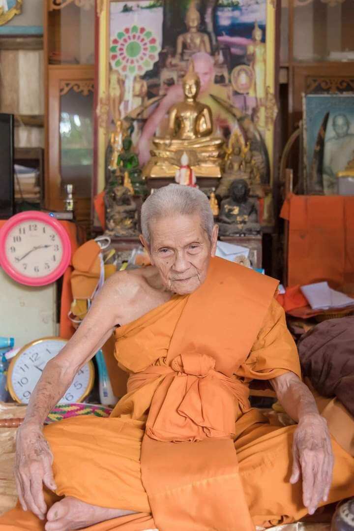 Elderly Thai monk seated in temple shrine with Buddha statue used to bless authentic Thai python skin talisman
