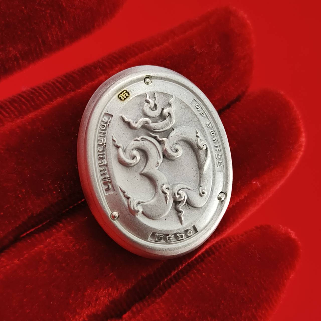 Sacred Ganesha talisman for fortune in a silver finish displayed on a red velvet background.
