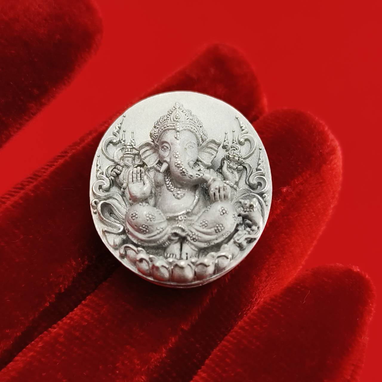 Sacred Ganesha talisman for fortune featuring intricate design on a silver coin placed on a red velvet background