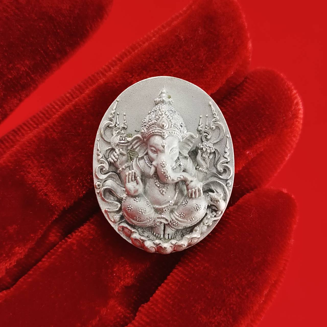 Sacred Ganesha talisman for fortune in intricate silver design held on a red velvet background