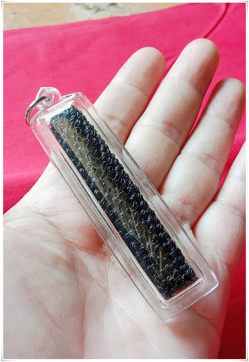 Sacred Thai amulet for good fortune held in hand, enclosed in a protective case.