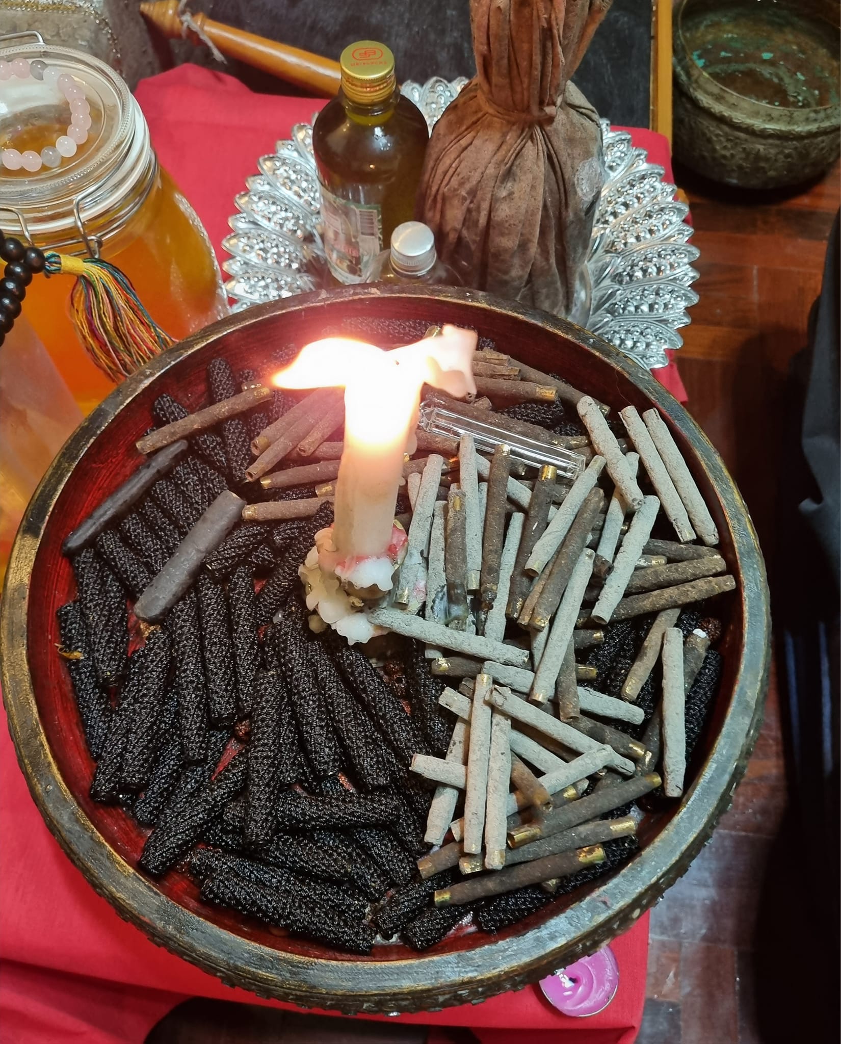 Sacred Thai amulet for good fortune displayed with candles and herbs in a decorative bowl