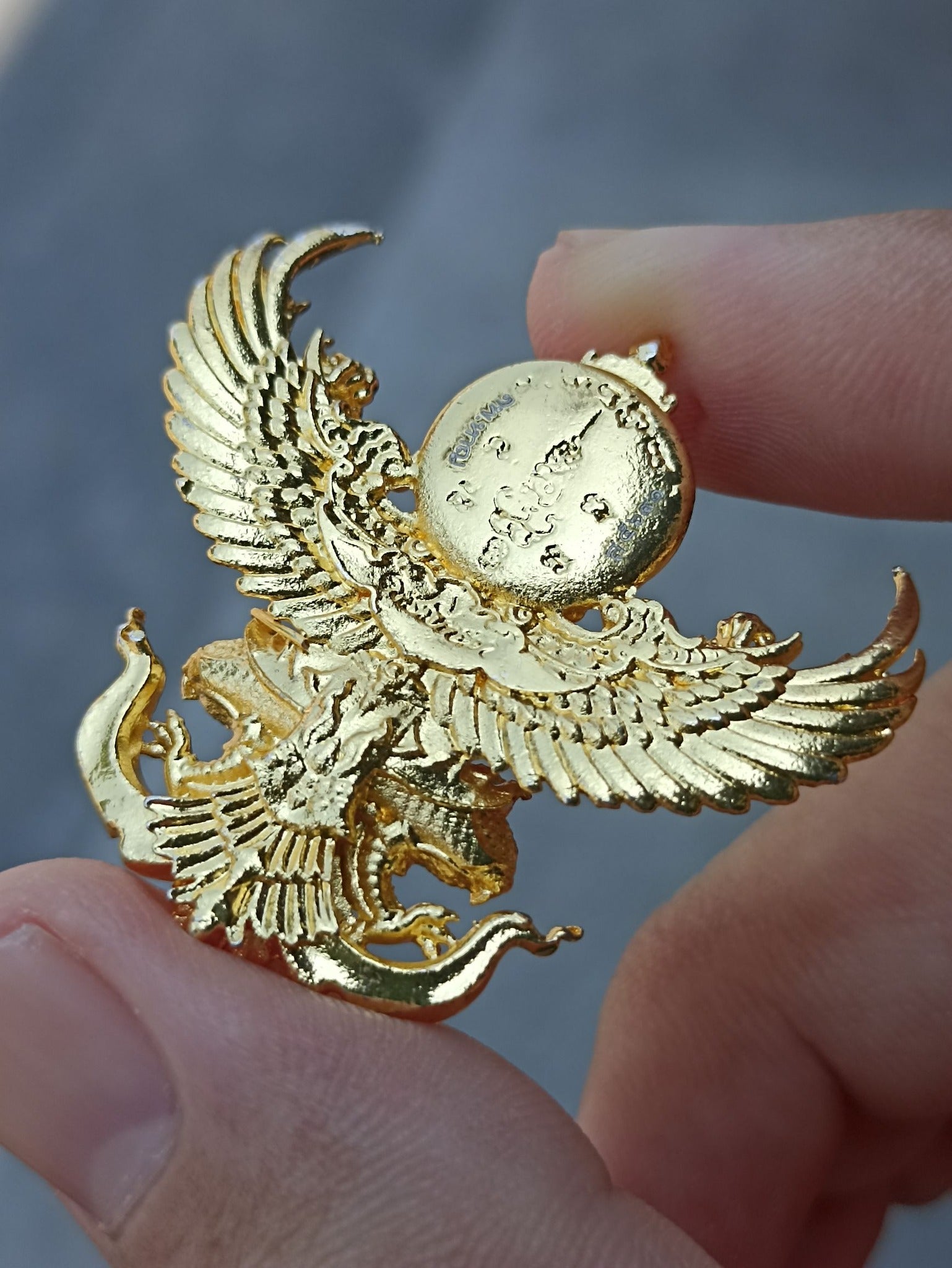 Close-up of a Sacred Thai elephant-bird amulet held by fingers, showcasing intricate gold detailing