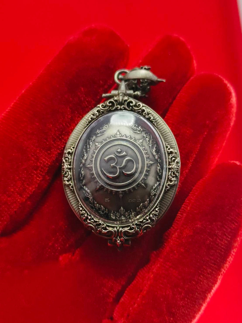 Thai Ganesh pendant white satin gold ornate oval amulet with Om symbol in decorative metal frame on red velvet background