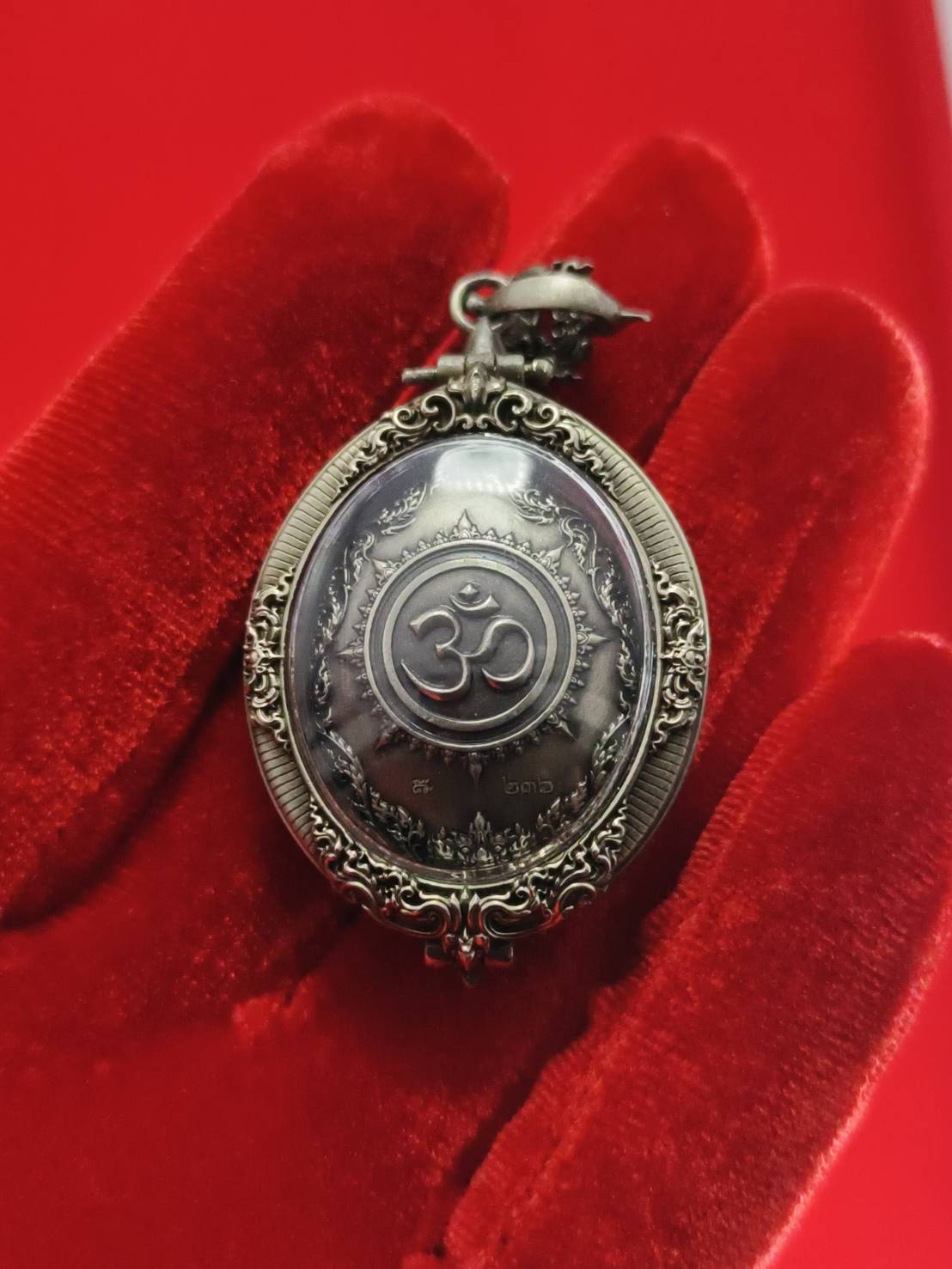 Thai Ganesh pendant white satin gold ornate oval amulet with Om symbol in decorative metal frame on red velvet background