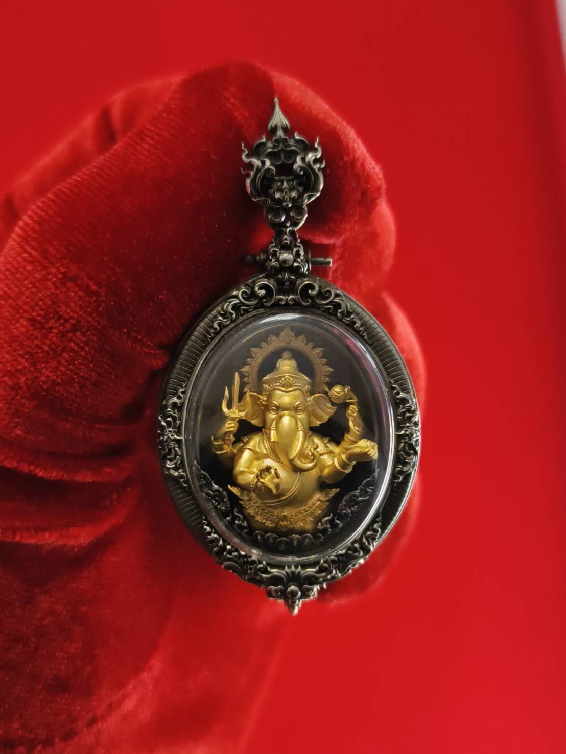 Thai Ganesh pendant white satin gold ornate oval amulet with gold Ganesha in antique silver frame on red glove background