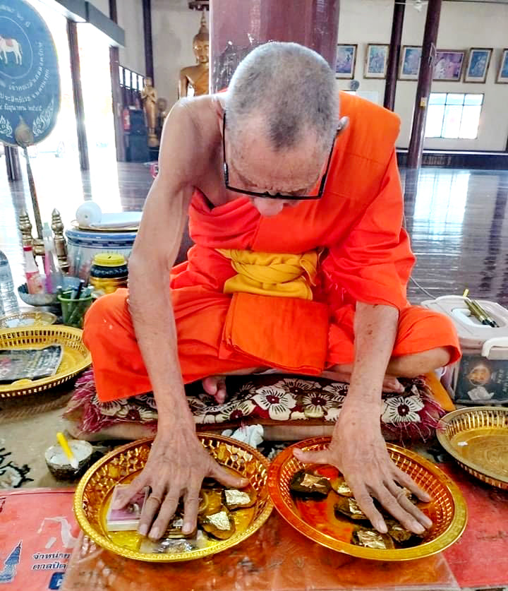 Monk blessing Thai wild cat placenta amulet on golden trays in Thai temple for protection and luck