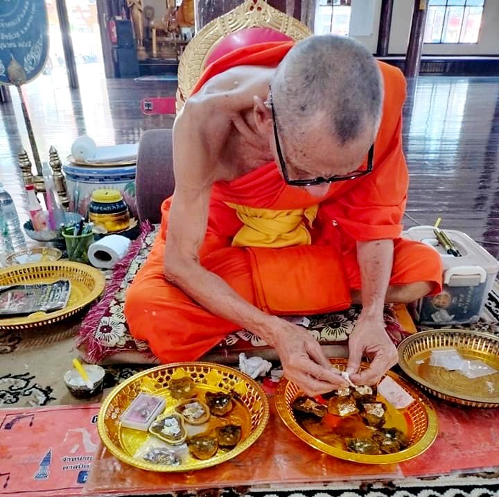 Buddhist monk inspecting golden trays of Thai wild cat placenta amulet offerings in temple setting