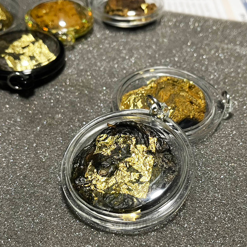 Thai wild cat placenta amulet in clear round case with dark placenta material and gold leaf flakes