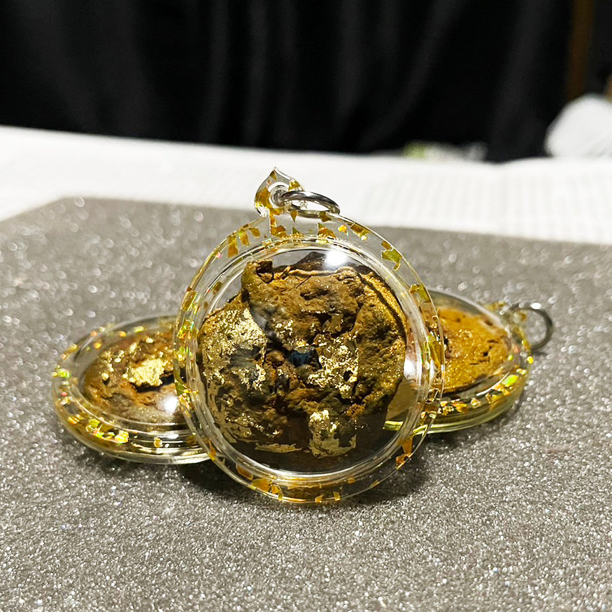 Thai wild cat placenta amulet in clear round casing with gold leaf flakes three amulets on glittered surface