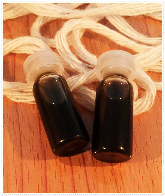Two small dark glass vials with white caps on wood and braided white cord Thai Blessing Co passion oil for couples