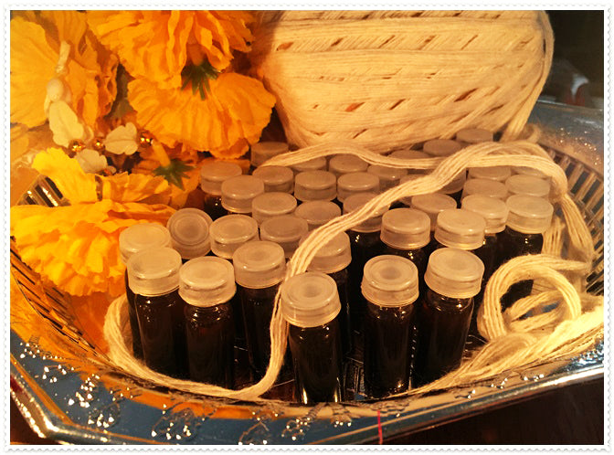 Small dark glass vials with white caps arranged in a woven basket with marigold flowers and twine passion oil for couples