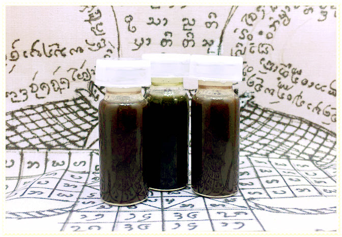 Three small glass vials of dark Thai blessing oil on script cloth labeled passion oil for couples