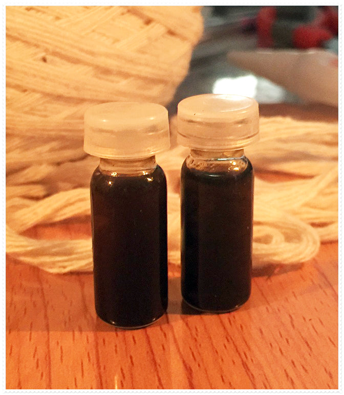 Two small glass vials of dark liquid with white caps on wooden table and yarn background passion oil for couples