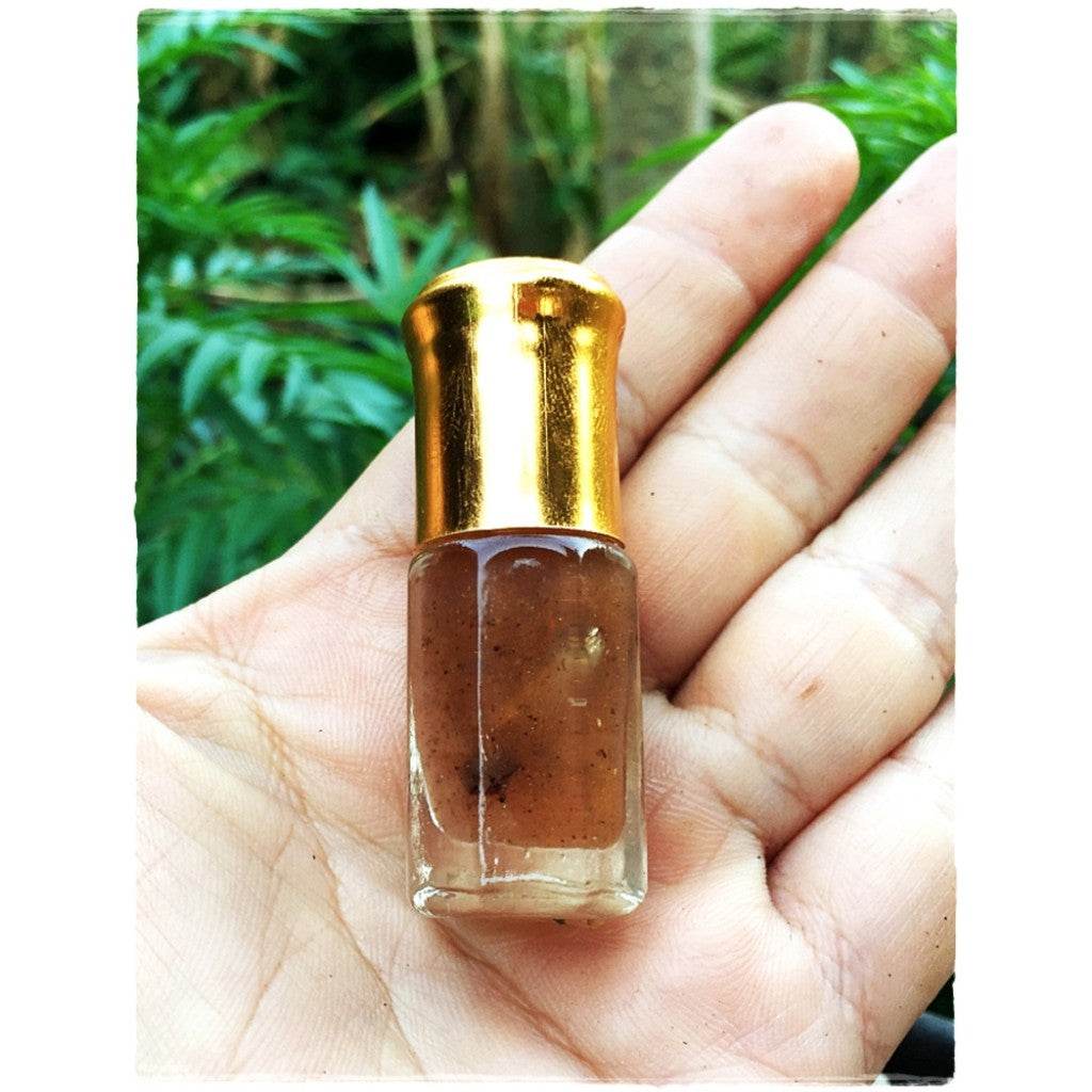 Small glass bottle of Thai love attraction oil with golden cap and brown speckled massage oil held in hand