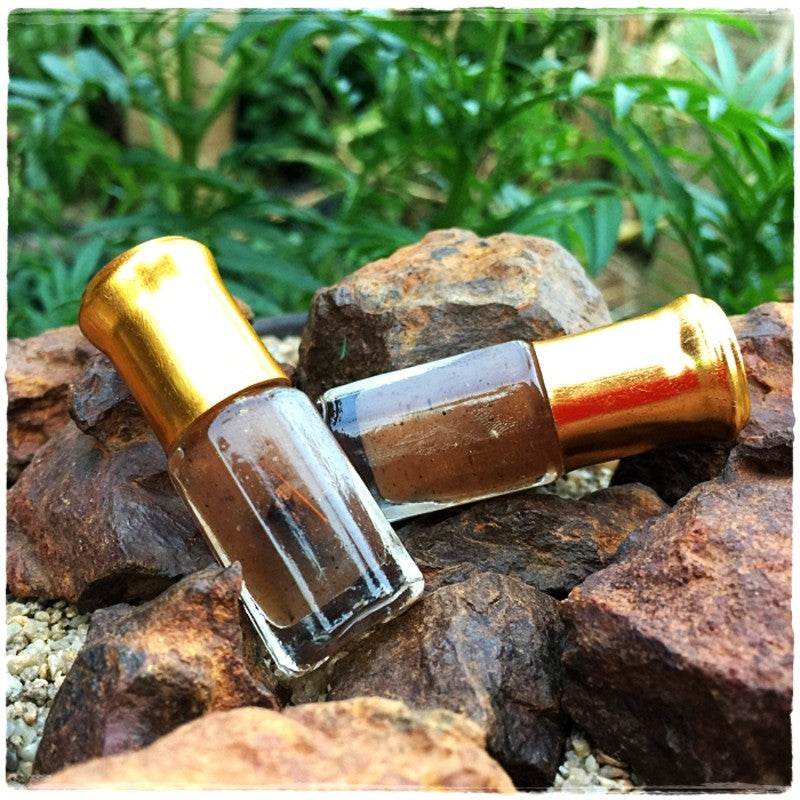 Thai love attraction oil in two small glass roller bottles with brown oil and gold caps on rocks outdoors