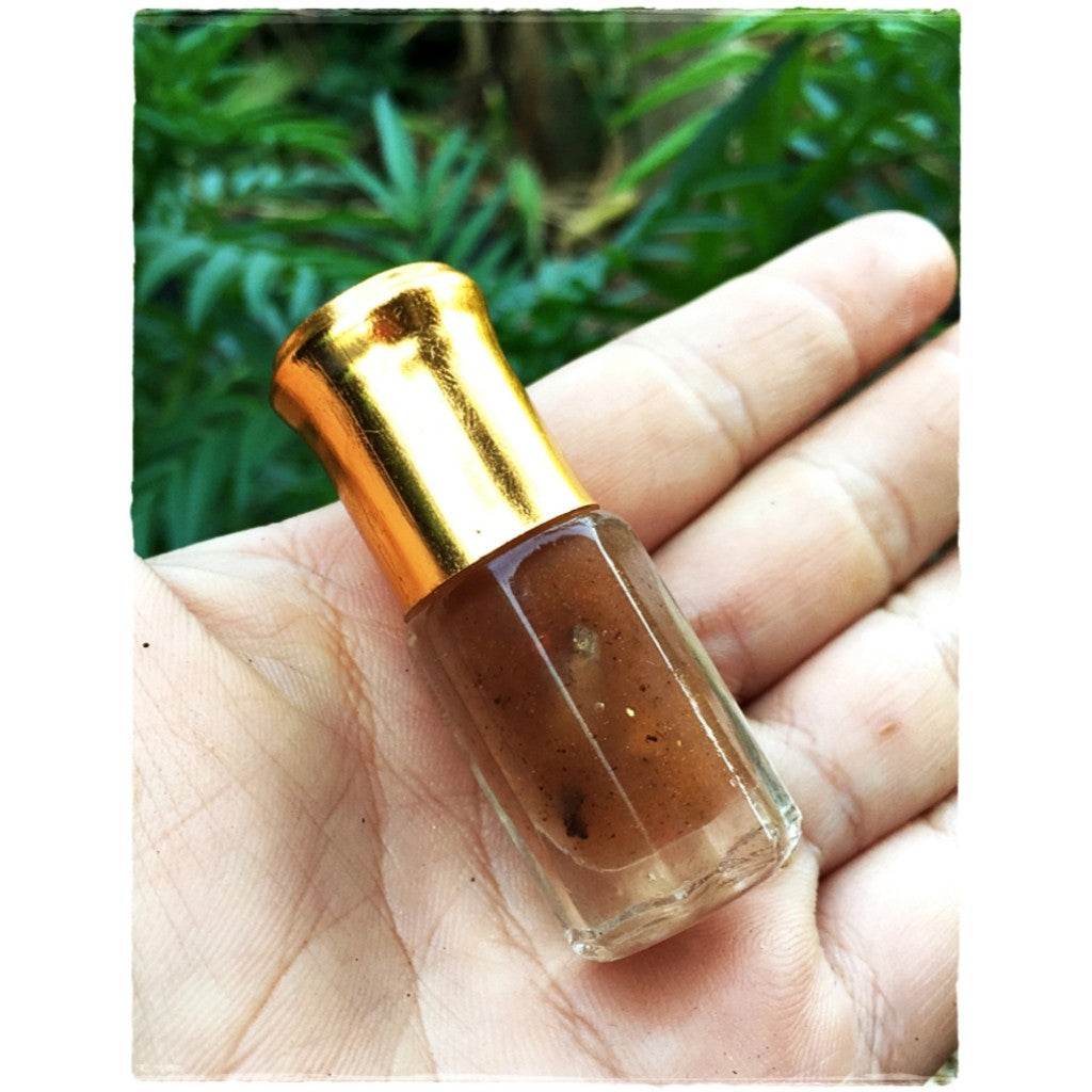 Small glass bottle of Thai love attraction oil with gold cap and brown herbal blend held in hand