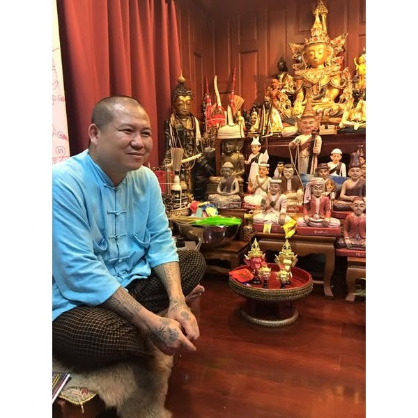 Man sitting in traditional Thai room with multiple religious statues and Thai golden face charm pendant on display