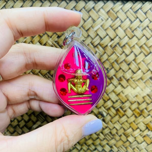 Hand holding Thai golden face charm pendant with red and purple background and decorative stones