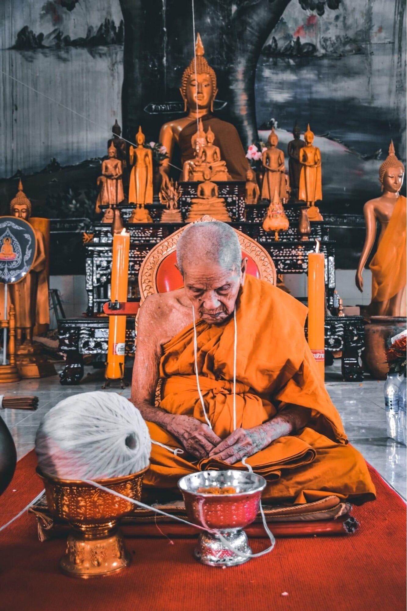 Monk blessing Phra Pidta Maha Uthom Amulet - Yung Yan (One of Siam's Sacred Symbols) amid Buddha statues