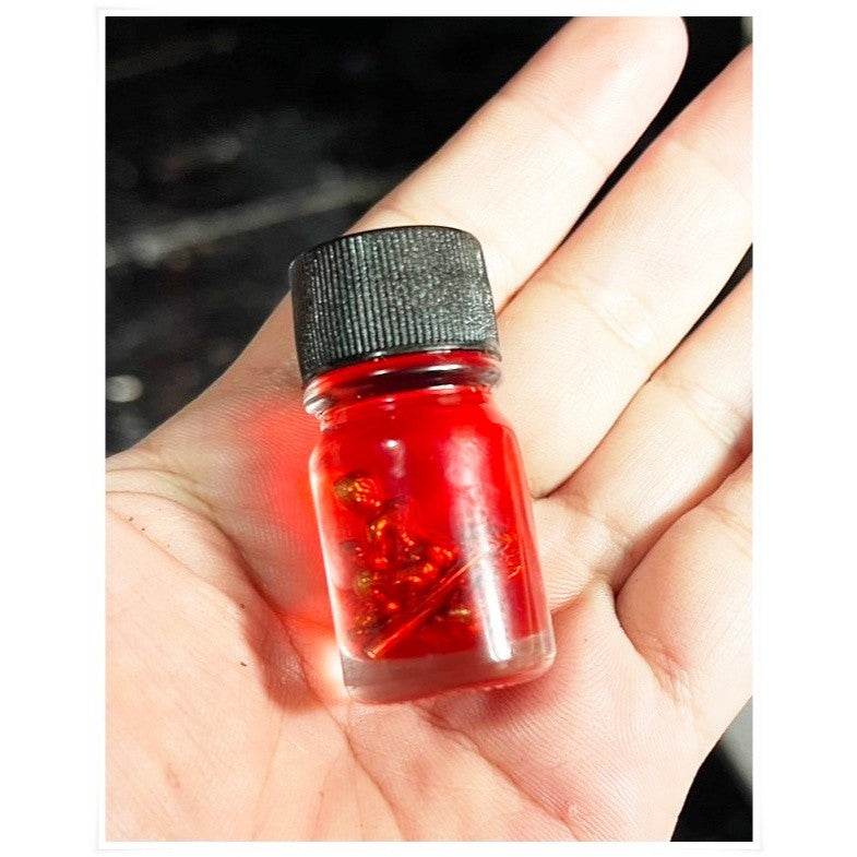 Small glass bottle of red Thai Blessing Co spiritual oil for rekindling love with sparkling herbs inside