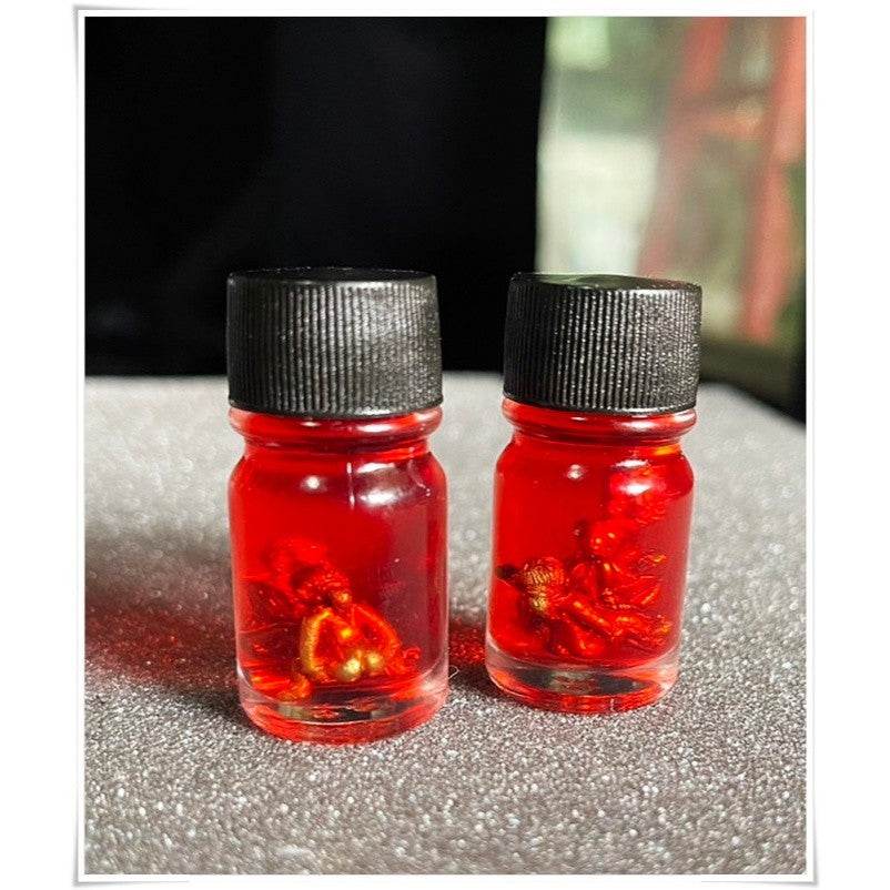 Two bottles of Thai Blessing Co spiritual oil for rekindling love with vibrant red liquid and decorative elements