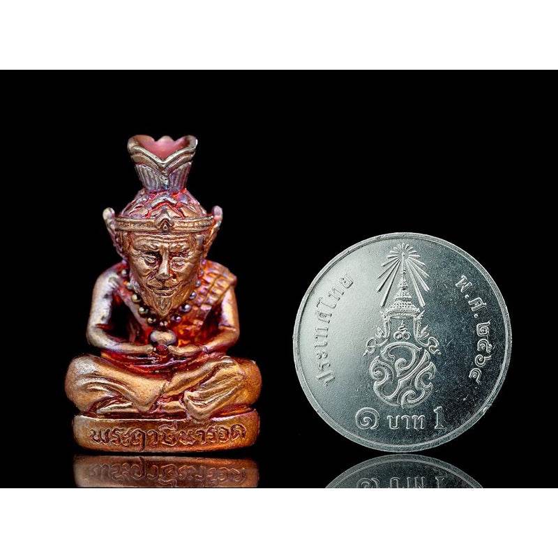 Supreme Ruesi Narot amulet in gold and bronze with detailed craftsmanship next to a Thai coin for scale