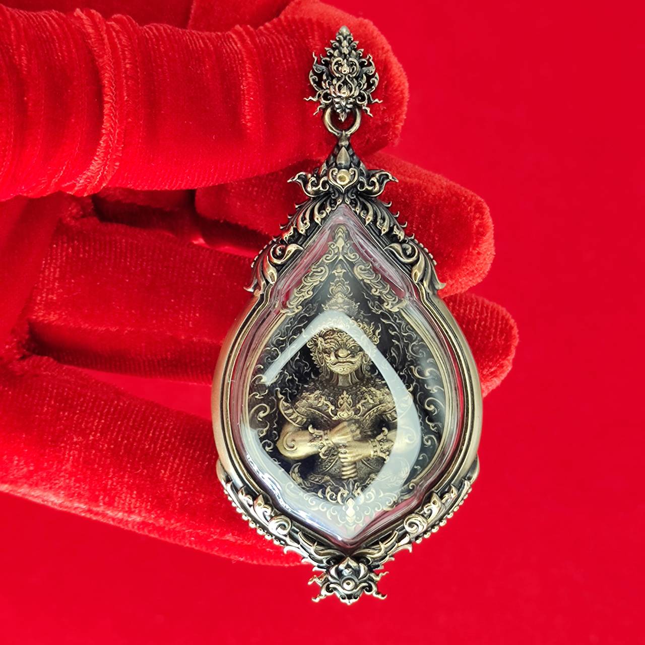 Tao Wessuwan amulet for protection displayed in ornate frame, held against a red background