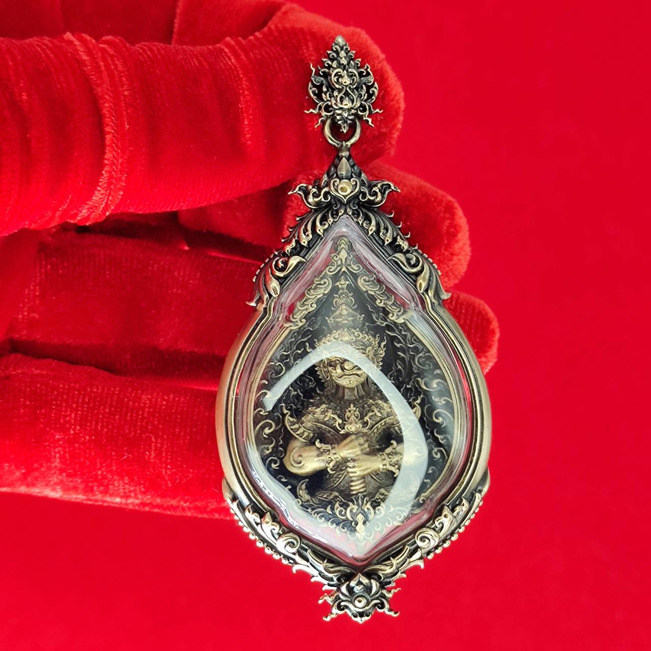 Tao Wessuwan amulet for protection in a decorative case held by a gloved hand, featuring intricate design.