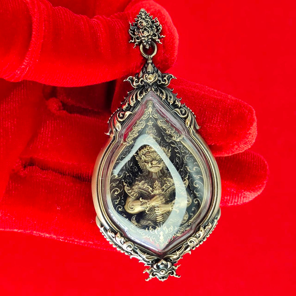 Tao Wessuwan amulet for protection in ornate silver casing, held by a red-gloved hand against a vibrant background