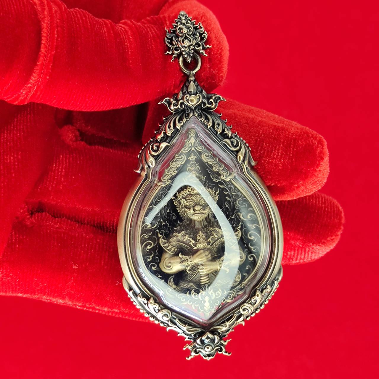 Tao Wessuwan amulet for protection in ornate silver casing, held by a red-gloved hand against a vibrant background