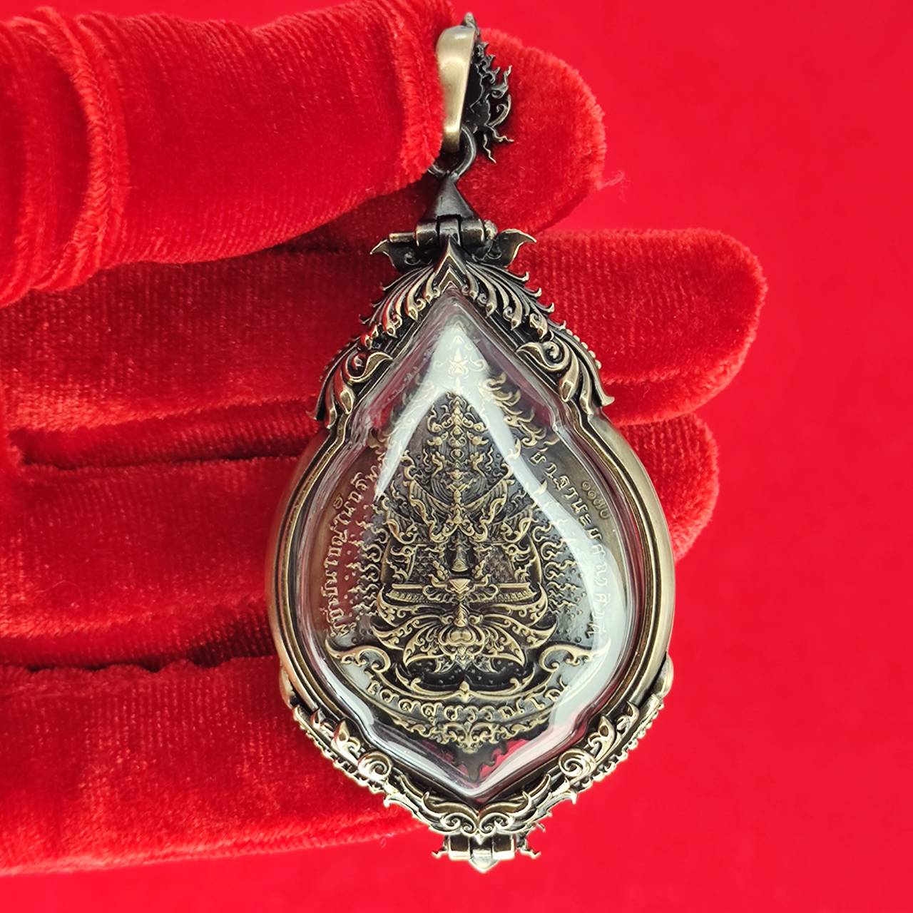 Thai Blessing Co Tao Wessuwan amulet for protection in ornate silver design, held against a vibrant red background