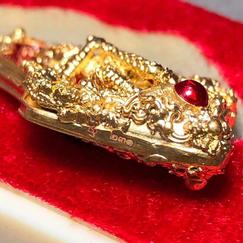 Tao Wessuwan amulet for wealth in gold with intricate designs and a red gemstone accent