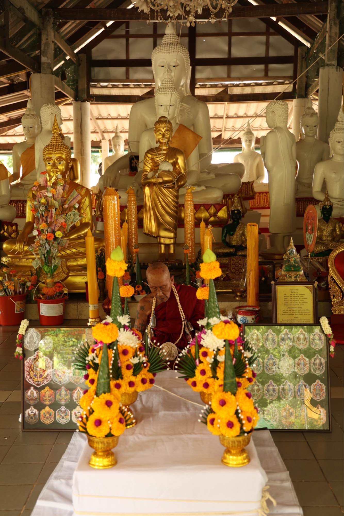 Tao Wessuwan Garuda amulet displayed in a serene temple setting with golden Buddha statues and floral decorations