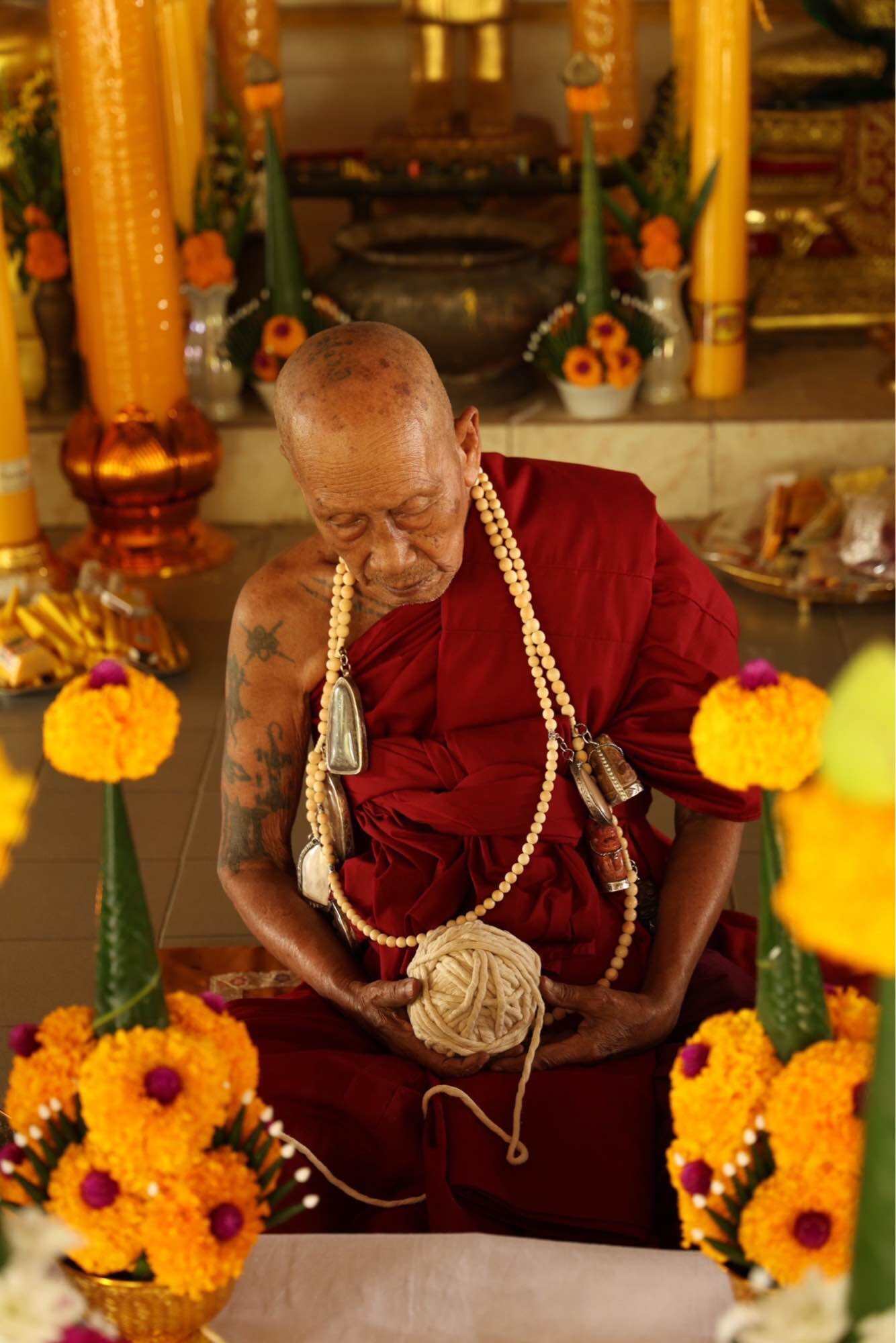 Monk creating a Tao Wessuwan Garuda amulet surrounded by vibrant flowers and sacred decorations