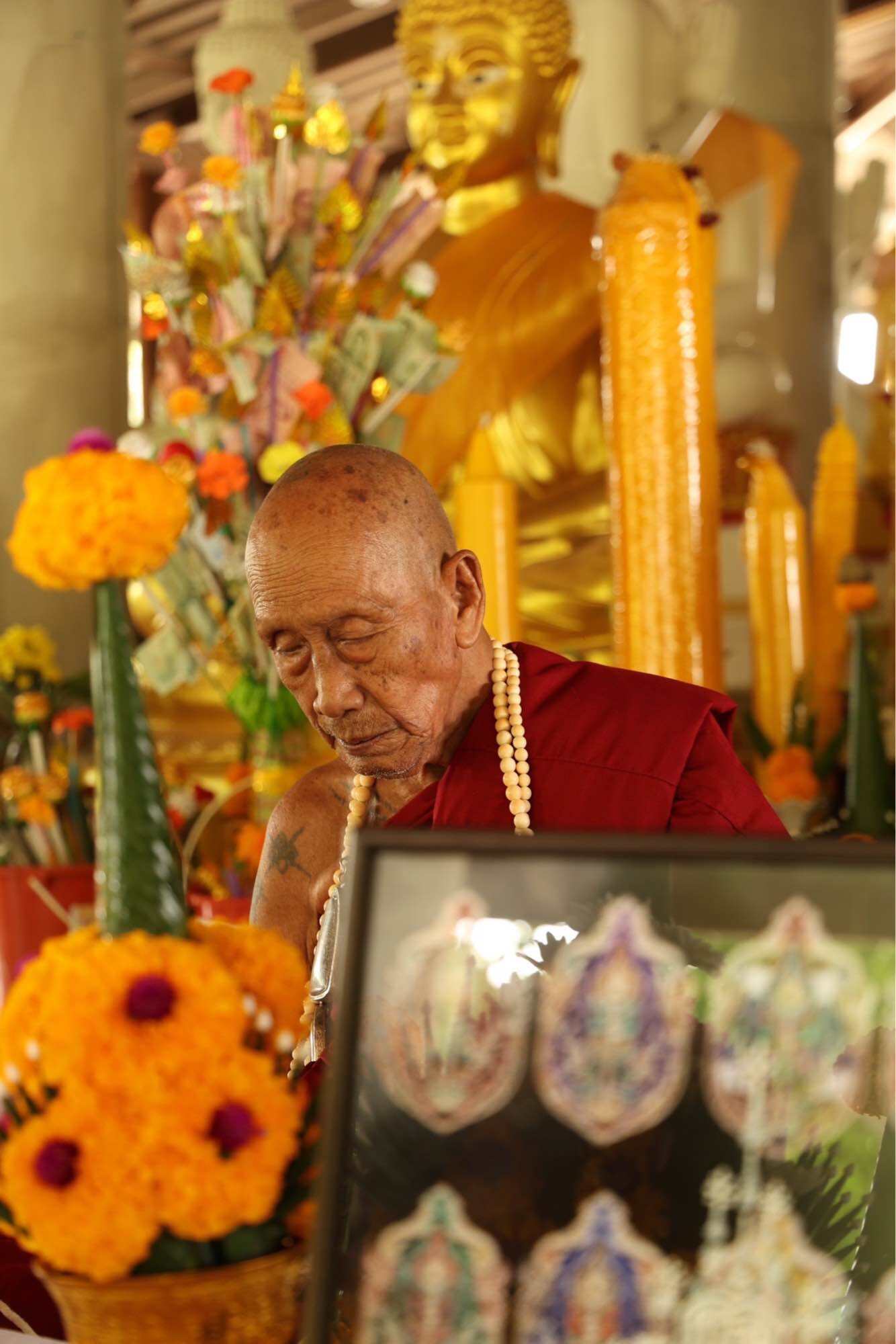 Tao Wessuwan Garuda amulet displayed at a temple with floral decorations and a monk in the background