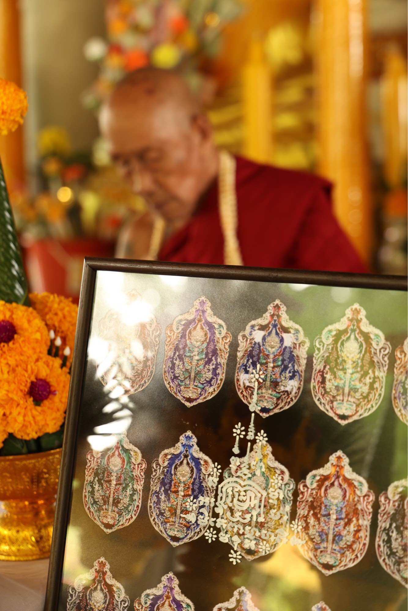 Tao Wessuwan Garuda amulet display with vibrant designs and a monk in the background at a temple setting