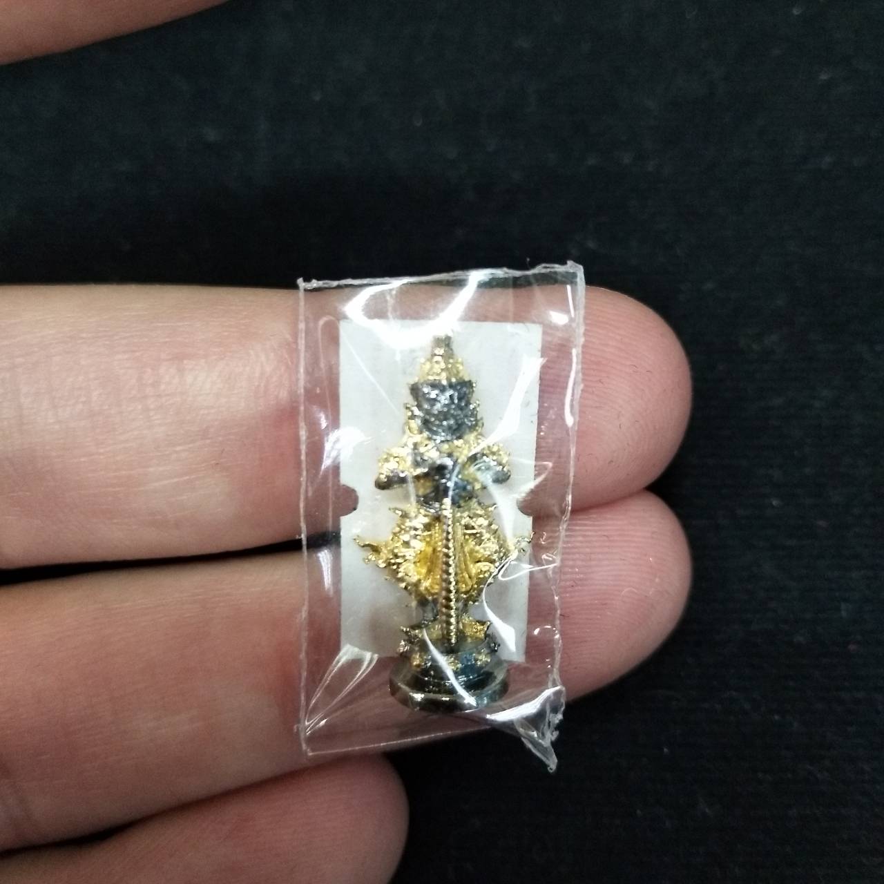 Taow Wessuwan amulet for wealth in protective casing held between fingers for spiritual collectors