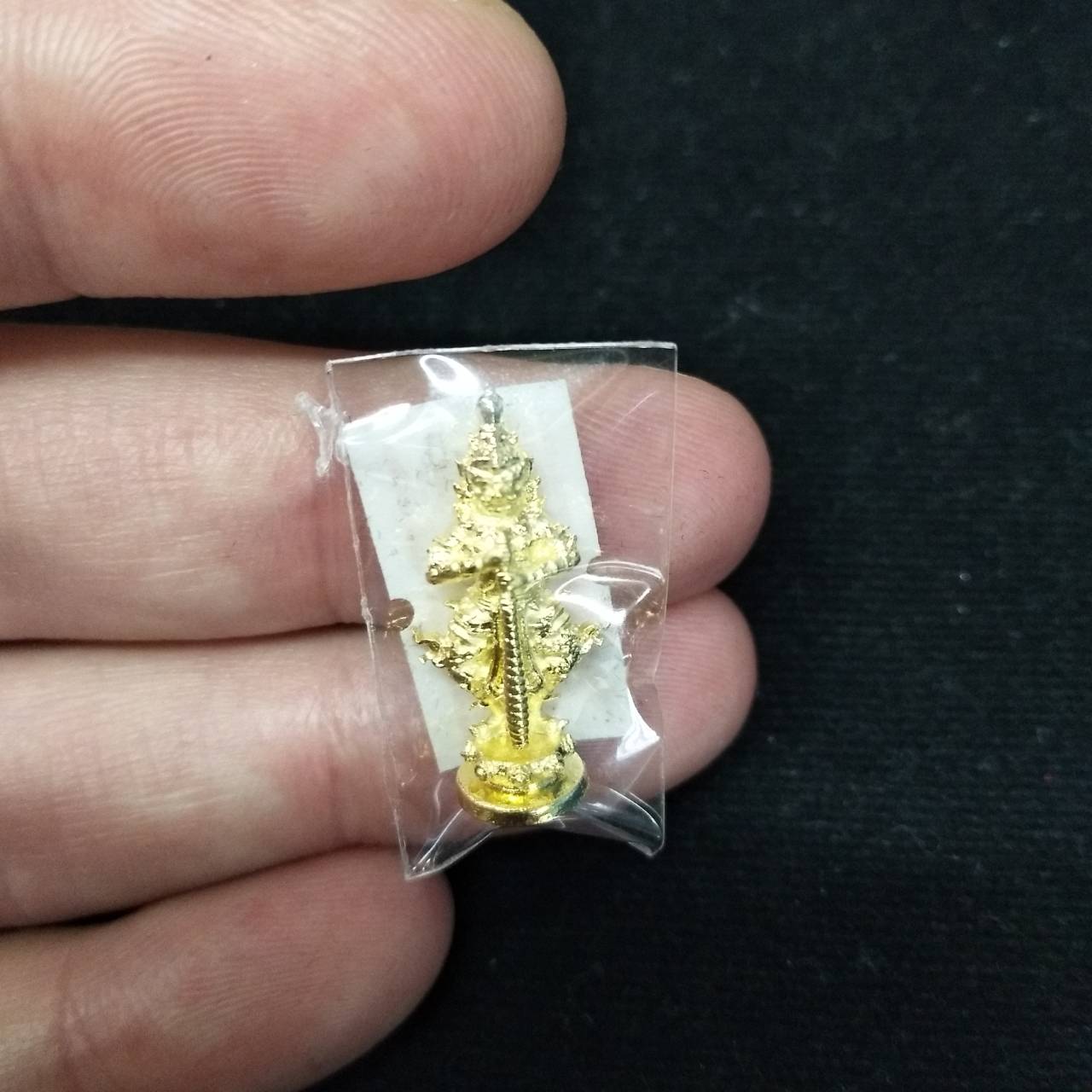 Taow Wessuwan amulet for wealth in gold, held in a clear package for protection and display