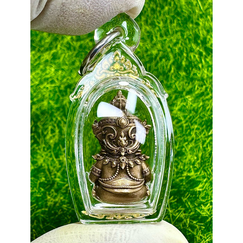 Taowessuwan amulet blessed by monk in clear protective casing held against green background