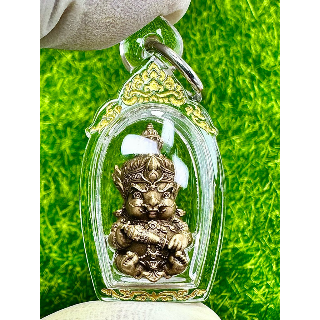 Taowessuwan amulet blessed by monk in clear protective casing with gold detailing held against green background