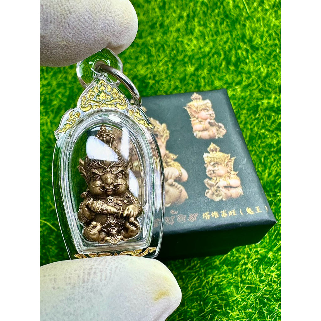 Taowessuwan amulet blessed by monk in protective clear case held over green surface with decorative box