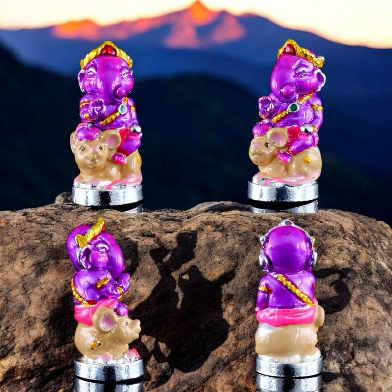 Ganesha blessing amulet Thailand in purple and gold sitting on a beige mouse base atop a rock with mountains in background
