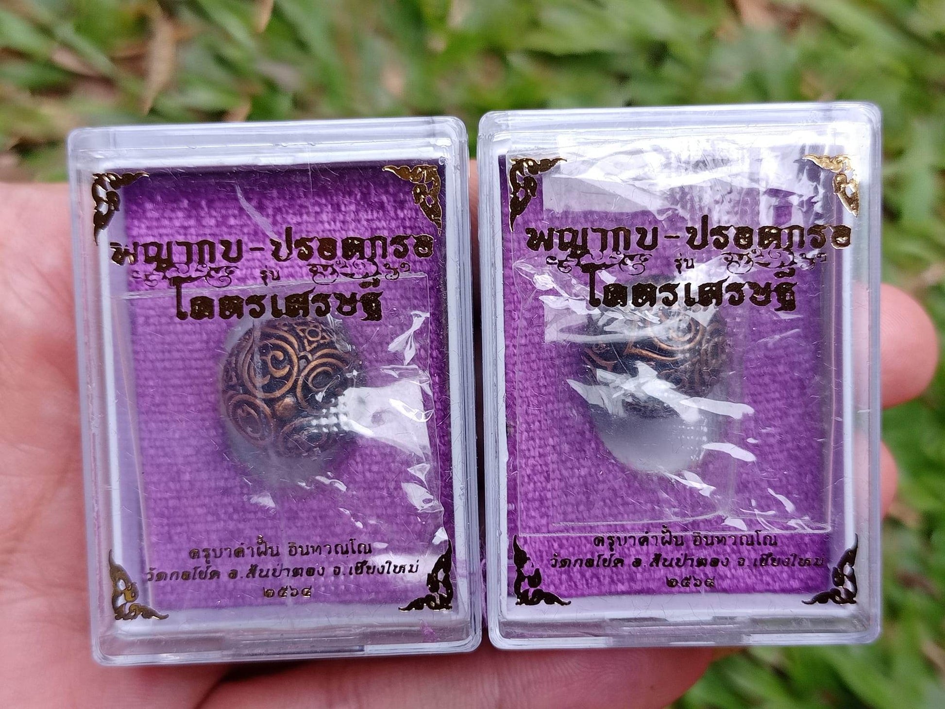 Pair of Thai Blessing Co ancient mercury spirit orb amulets in clear plastic display boxes with purple backing