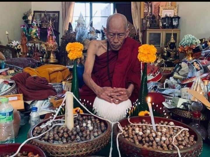 Elderly man in red robe in ceremonial room with bowls of ancient mercury spirit orb beads and offerings