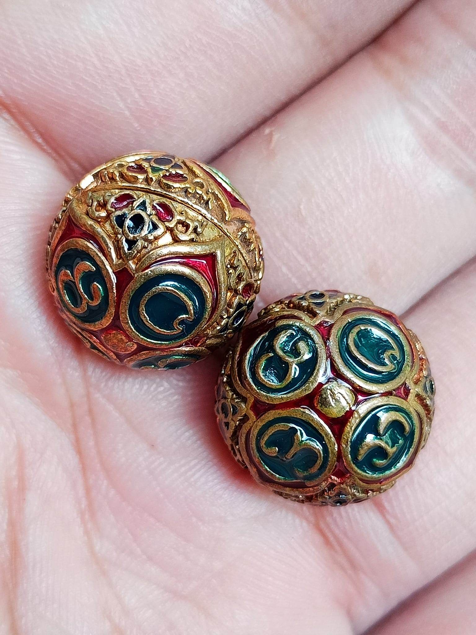 Two ornate Thai blessing amulets in a palm with gold filigree and green enamel ancient mercury spirit orb for feng shui
